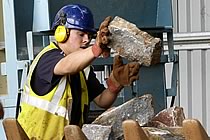 Man in blue hard hat and reflective jacket checking handling a large limestone block.